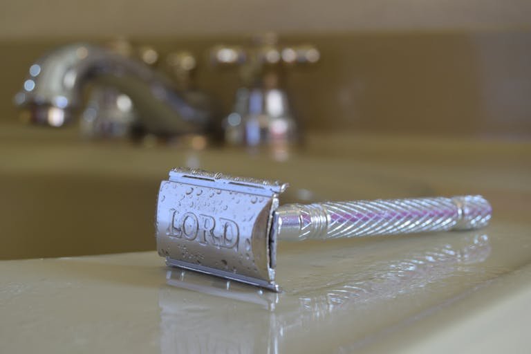 Sharp wet razor resting on a bathroom sink surface, showcasing its metallic finish.