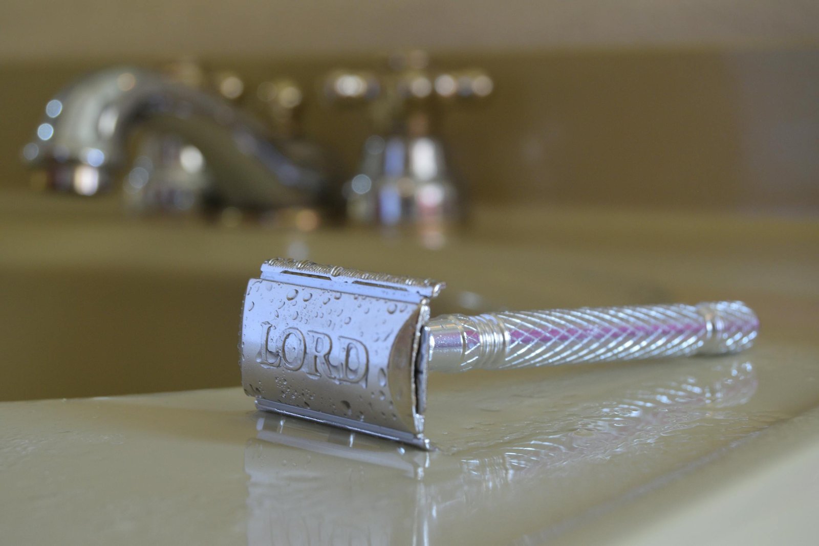 Sharp wet razor resting on a bathroom sink surface, showcasing its metallic finish.
